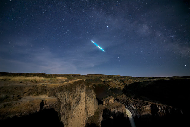A shooting star appears over Palouse Falls on a moonlit night, Southeast Washington, Washington State. Shadow of the photographer appears in the lower left hand corner.