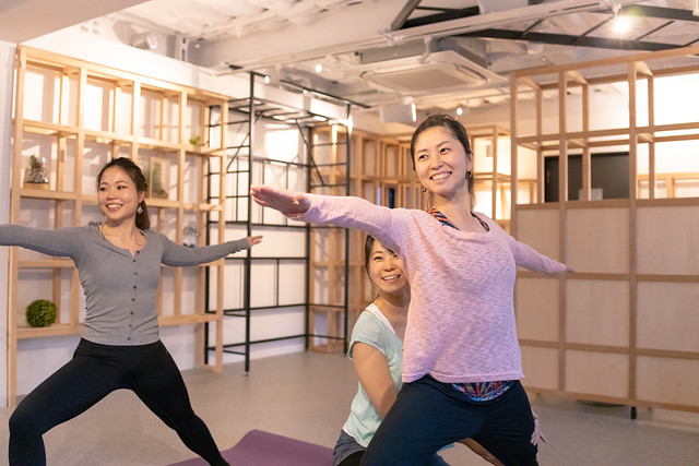 Professional yoga instructor supporting woman in health club