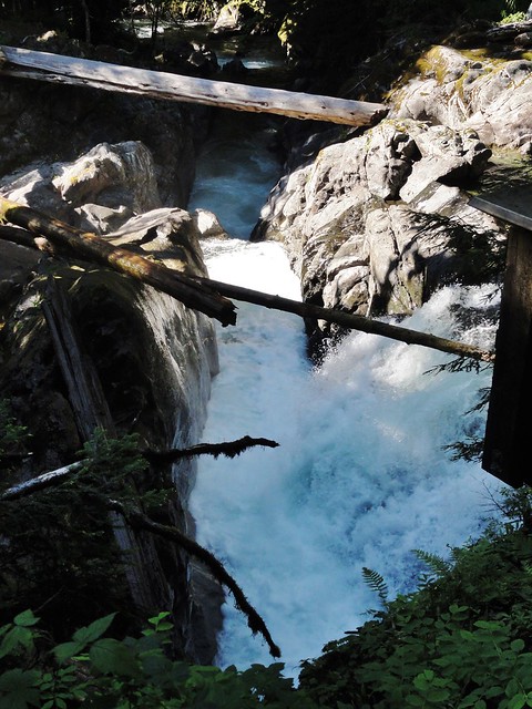 Photograph shows a waterfall plunging at the right, into a channel that flows away at a right angle from it. 