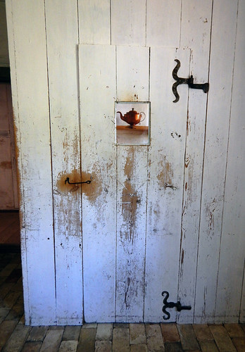 An old door with a cut-out that reveals a copper kettle in a recreation of an 1864 kitchen
