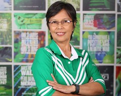 The image shows ASP National secretary Ms. Cecile Sicam standing in front of ASP Hugot wall wearing glasses and ASP uniform. She has black short hair.