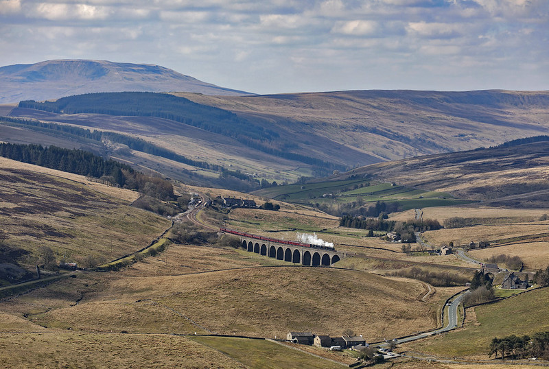 44871 & 45407 The Lancashire Fusilier cross Dandry Mire Viaduct at Garsdale Head, starting the final ascent to Ais Gill Summit, with The Citadel

The trackbed of the old line to Hawes can be seen branching off to the left. In the middle distance and lower right hand side are the Midland Railway cottages, 22 in total. The roof of Mount Zion chapel is just above the railway bridge over the road, and in the foreground is the Moorcock Inn. Garsdale station platforms are visible next to the railway cottages, with the signal box prominent on the northbound side and semaphores both north and south of the station. The platform that used to be used for the Hawes branch trains can be seen on the left of the station, the trackbed now tarmacked over. The location of the station in its isolated and elevated position above the valley can be appreciated.

Great Coum, with its summit at 687 metres above sea level, overlooks the scene (thanks again to Andrew ARG_Flickr for the mountain info)