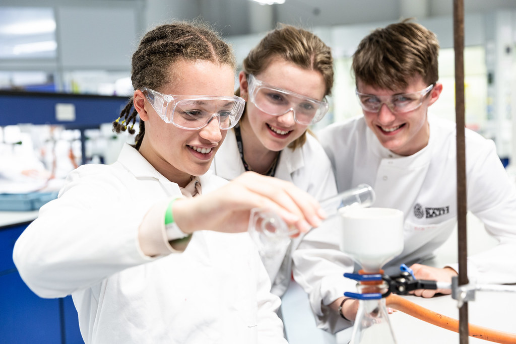 Three smiling school pupils undertake a lab test.