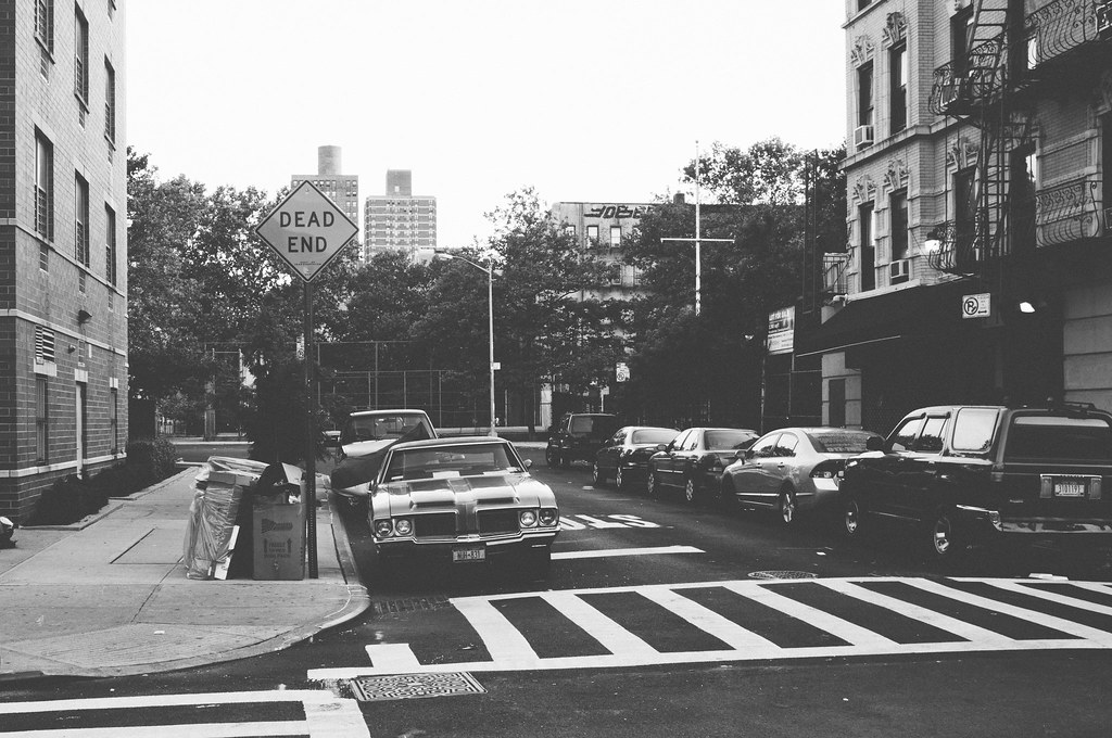 East Village street corner with a 'DEAD END' sign, crosswalk, and vintage Oldsmobile by brick tenements.