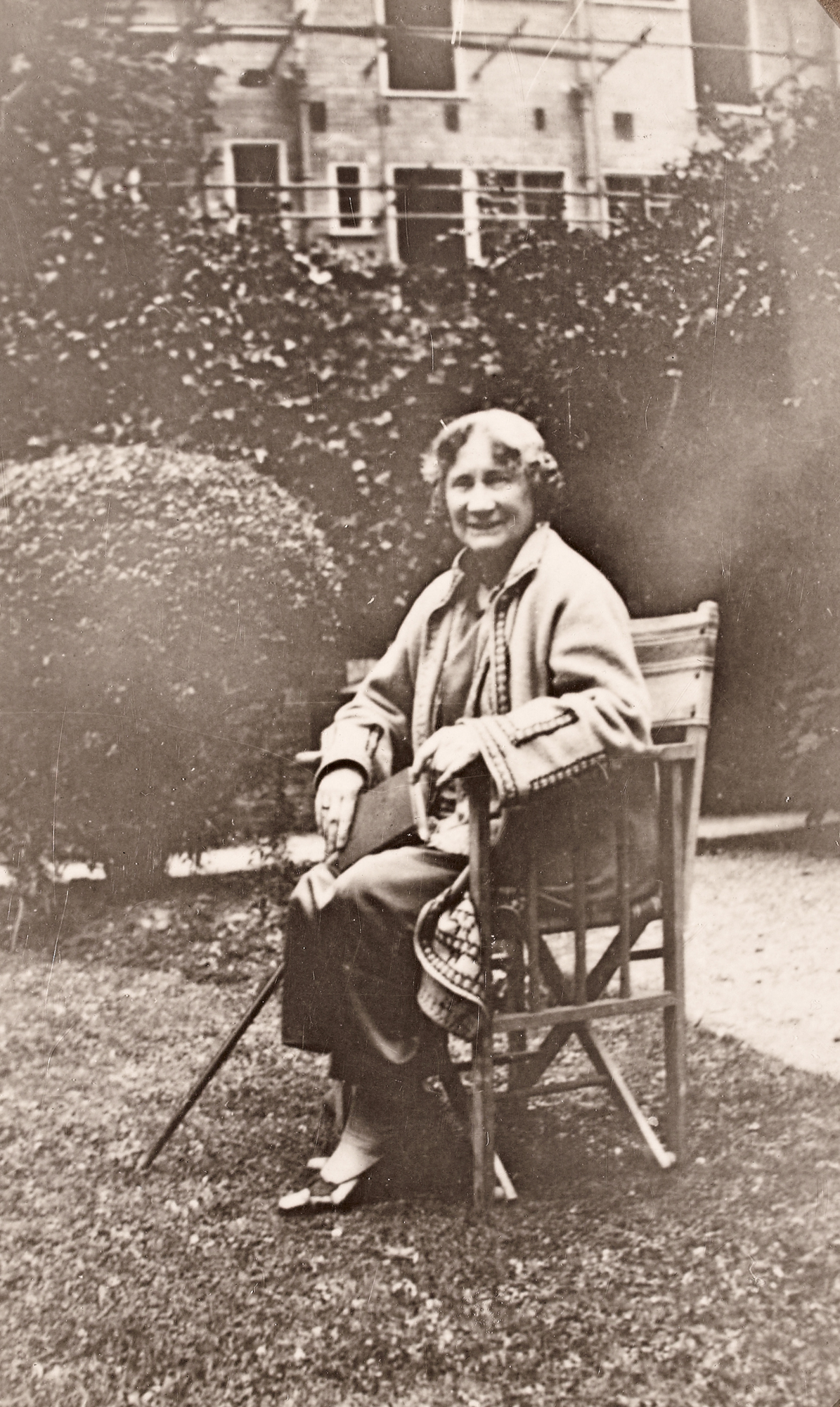 Eleanor Hull, full-length portrait seated in chair, in a garden with a book and a cane
