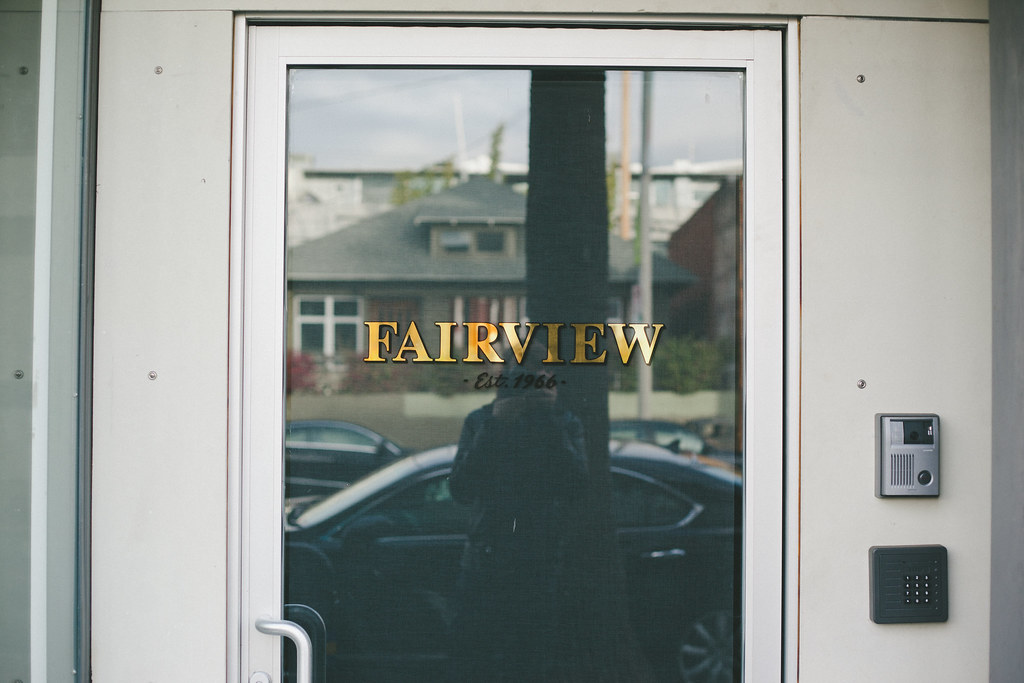 Glass entryway door with gold lettering reading 'FAIRVIEW - Est. 1966 -' reflecting street trees.