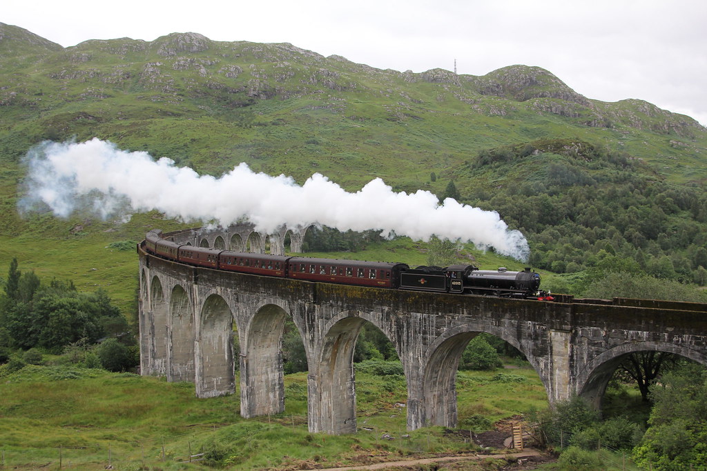 Steam train crossing Glenfinnan Viaduct among green hills