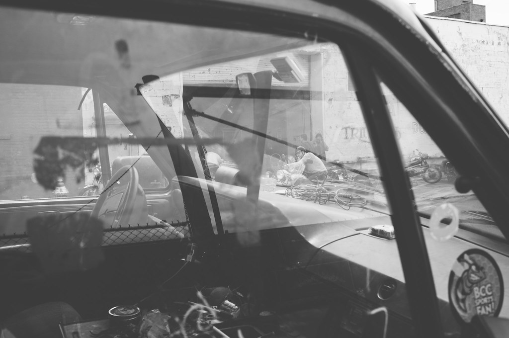 Windshield view of vintage motorcycles parked outside a Brooklyn workshop with Triumph signage.