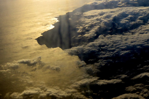 The Land of Clouds and Shadows giving way to The Sea of Gold by Snorkle-suz, Flying view, taken at sunset as we leave the Island I live on. 
I'm running away again, just for a w
