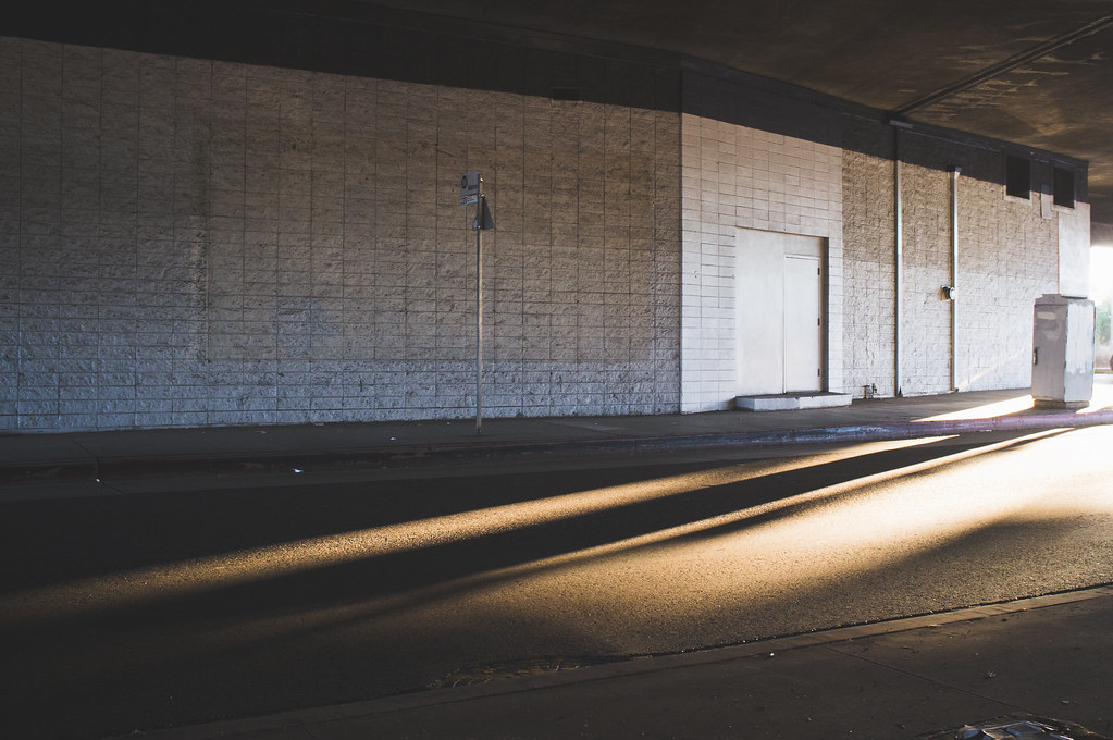 Concrete underpass wall and bus stop sign illuminated by streaks of golden afternoon sunlight.
