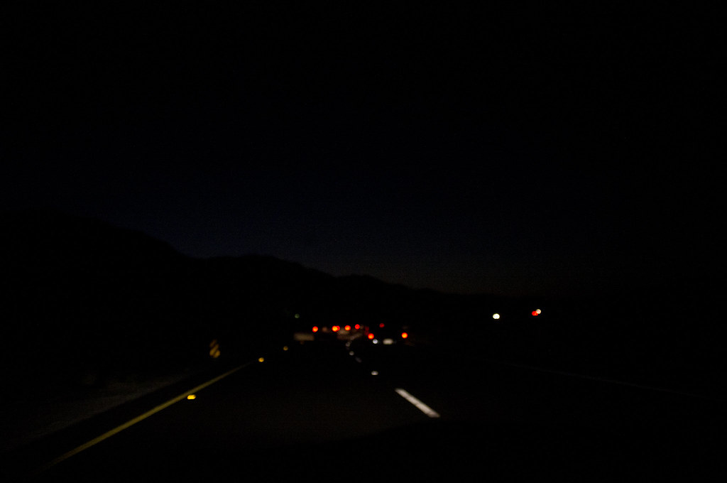 Night highway driving view showing vehicle taillights against silhouette of California mountains.
