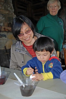 Small child sits on mother's lap while coloring on an egg with a blue crayon. 