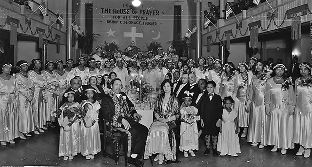 Daddy Grace and a group of men, women and children inside a House of Prayer for All People, 1930s