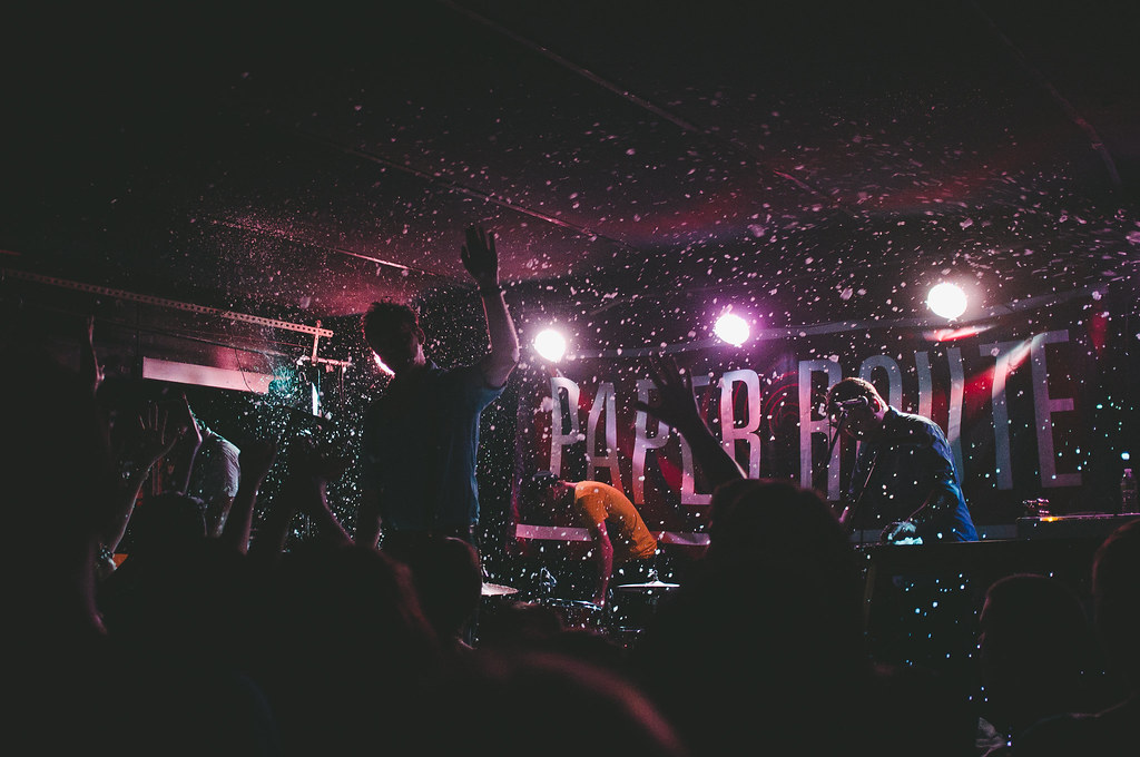 Band Paper Route performing on stage under spotlights amid falling white confetti and silhouettes.