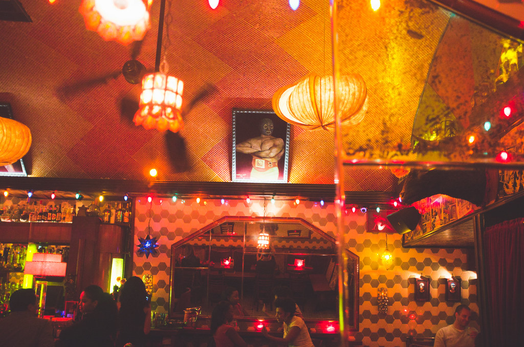 El Carmen bar interior adorned with glowing lanterns, lights, and a framed lucha libre portrait.