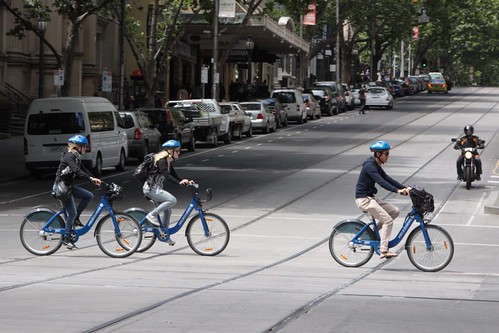 Trio of tourists head down Swanston Street with hired Melbourne Bike Share bikes and helmets