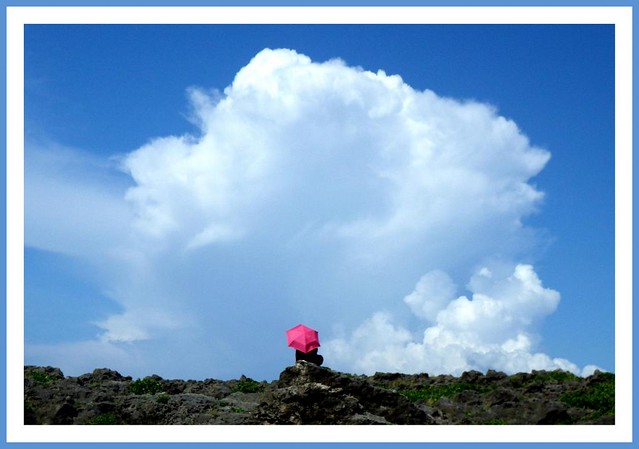 GIRL WITH A RED UMBRELLA SITTING ON A ROCK WHILE WATCHING A CLOUD