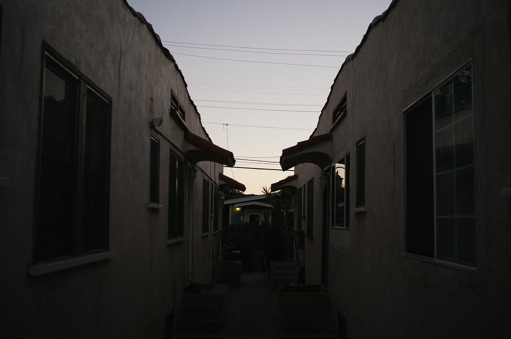Walkway between two rows of Spanish-style stucco apartment bungalows under an evening twilight sky.