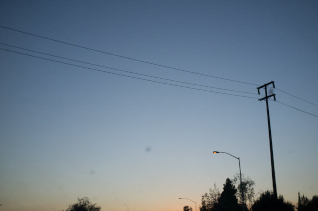 Minimalist roadside view of a utility pole and three power lines stretching across a calm dusk sky.