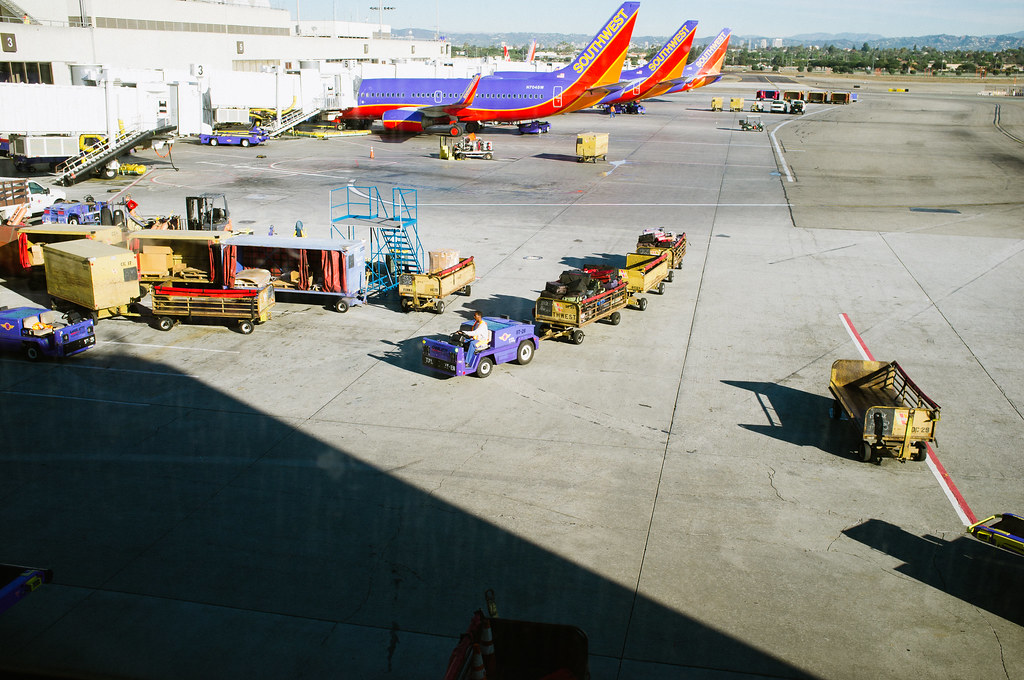 Baggage tug driving past parked Southwest Airlines planes at the gate during airport operations.
