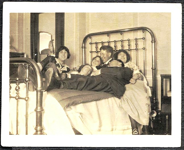 Four girls and two men in a big brass bed -- photo marked …