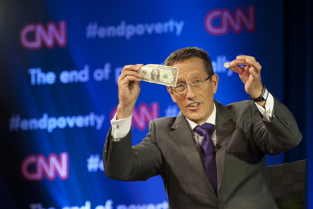 Richard Quest CNN  International Business Correspondent holds $1.25 in his hand, the amount the extremely poor live on each day