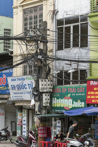 streetscene chaotic tangledwires oldbuildings shops motorcycles pedestrians seated woman signs cityculture hanoi vietnam