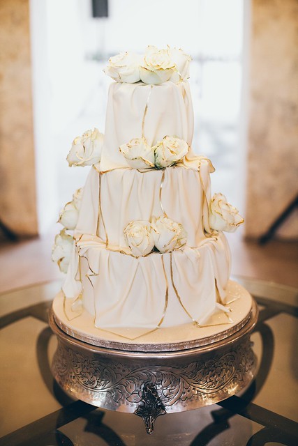 3-tier wedding cake (Wicked Chocolate flavour) iced in white chocolate ganache covered with ivory fondant drapes edged gold, decorated with fresh roses