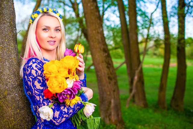 Fashion Concepts. Positive Smiling Caucasian Girl with Bunch of Fresh Colorful Tulips. Posing in Garland Outdoors in Spring Forest.